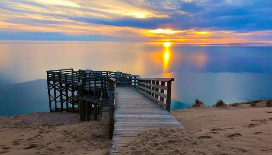 Dock leading into the water with a sunset of orange and blue colors. 